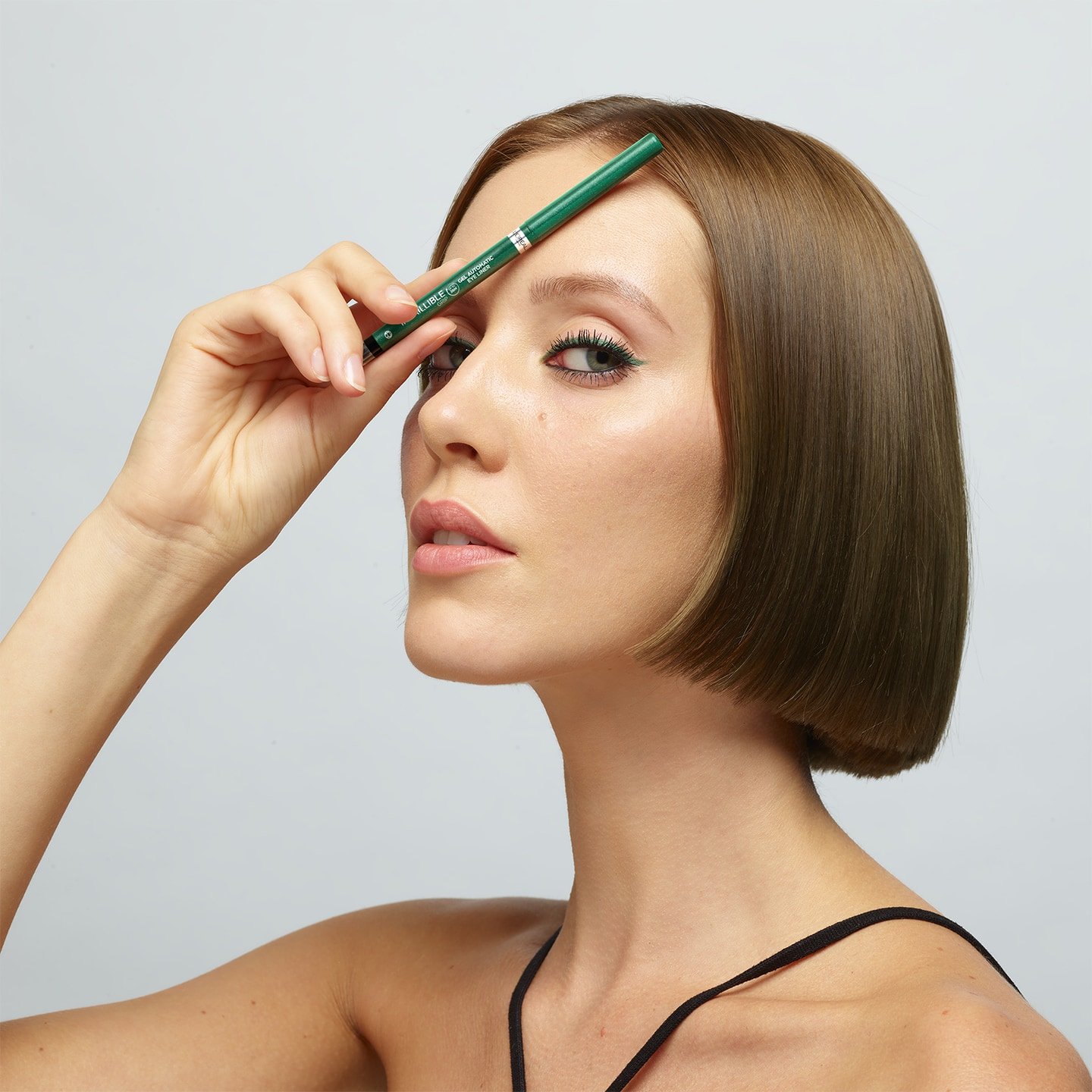 Eine junge Frau mit Make-up und halblangen Haaren hält sich den Grip Gel Automatic Eyeliner vor ihre Stirn
